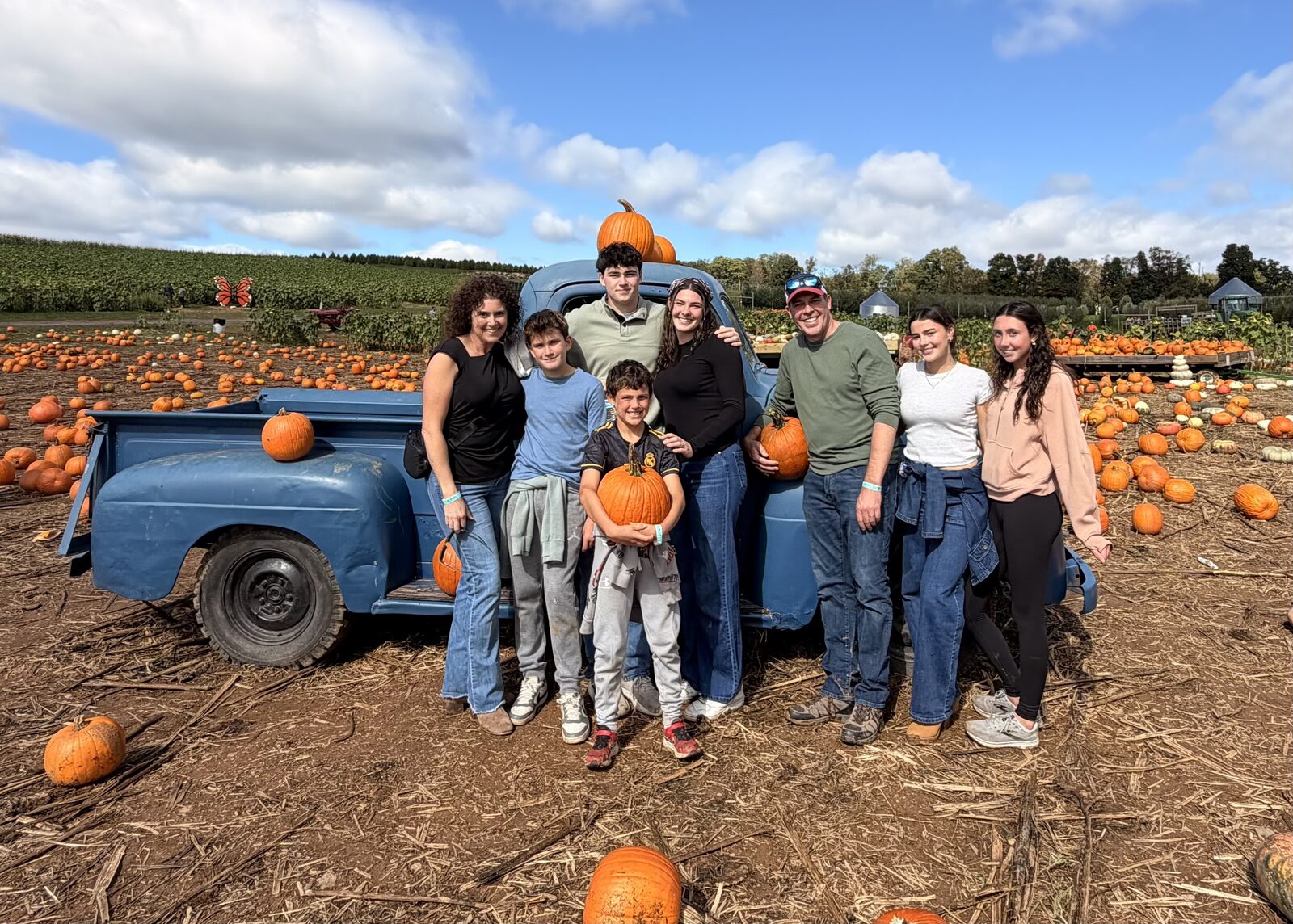 Ryan, Jeannie and their six kids with pumpkins and an old blue pickup at a pumpkin patch